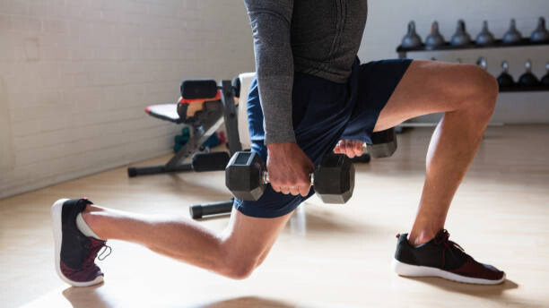 Na slici je prikazan muškarac koji radi iskorak sa bučicama - vežba za noge koja se može raditi kod kuće.