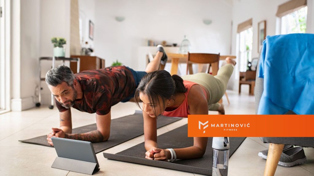 Na slici je prikazan par koji radi vežbe kod kuće - vežbe za grudi, ledja i noge.