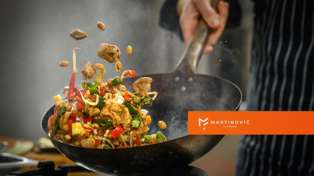 Na slici je prikazan kuvar koji sprema jelo u tiganju - kao naslovna slika na temu: kako smanjiti glad tokom procesa mršavljenja.