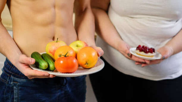 Na slici je osoba sa ravnim stomakom koja nudi tanjir svežeg voća, pored gojazne osobe sa tanjirom u kome je slatkiš.