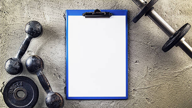 Na slici su prikazane bučice i sveska za raspored treninga za vežbe kod kuće.