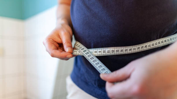 Slika prikazuje gojaznog čoveka koji meri obim struka.