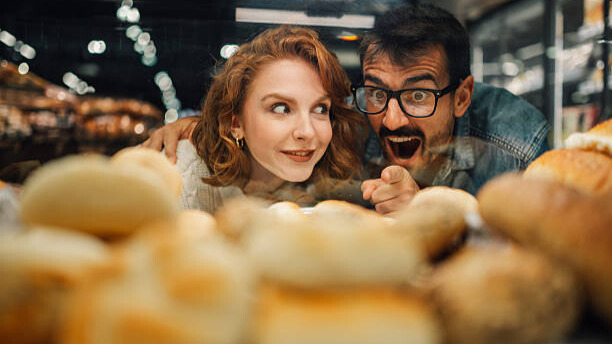 Na slici je prikazan par koji sa žudnjom posmatra hranu u vitrini.