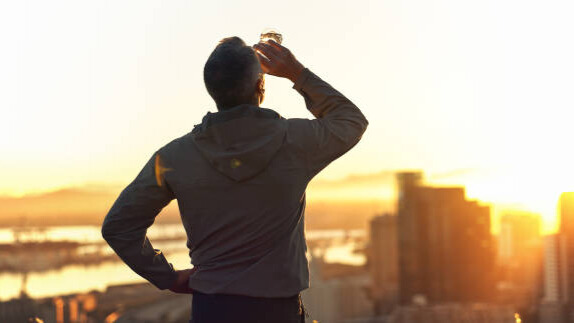 Na slici je muškarac koj nakon treninga uživa u zalasku sunca.