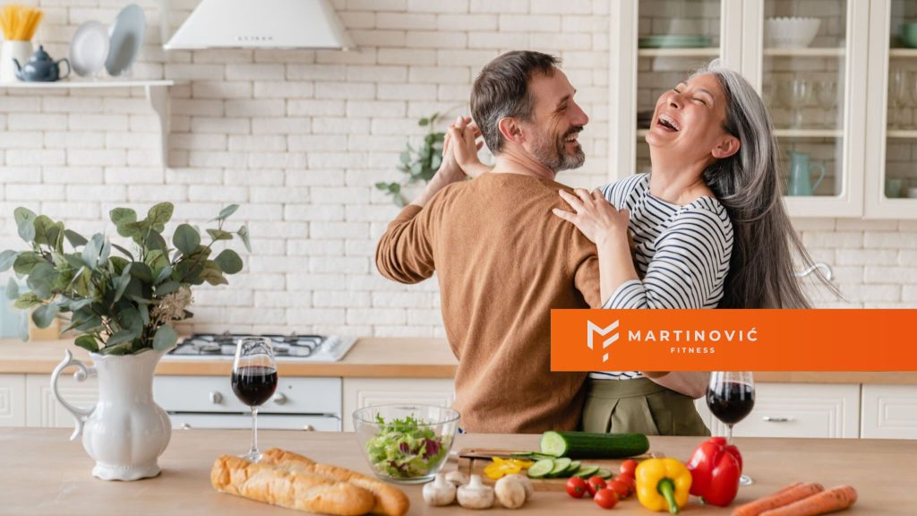 Na slici su muškarac i žena koji plešu u kuhinji.