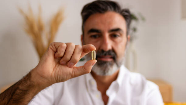 Na slici muškarac drži kaspulu vitamina D.