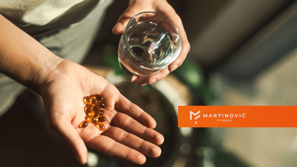 Na slici čovek drži u šaci suplement ishrani vitamin D, uz čašu vode.